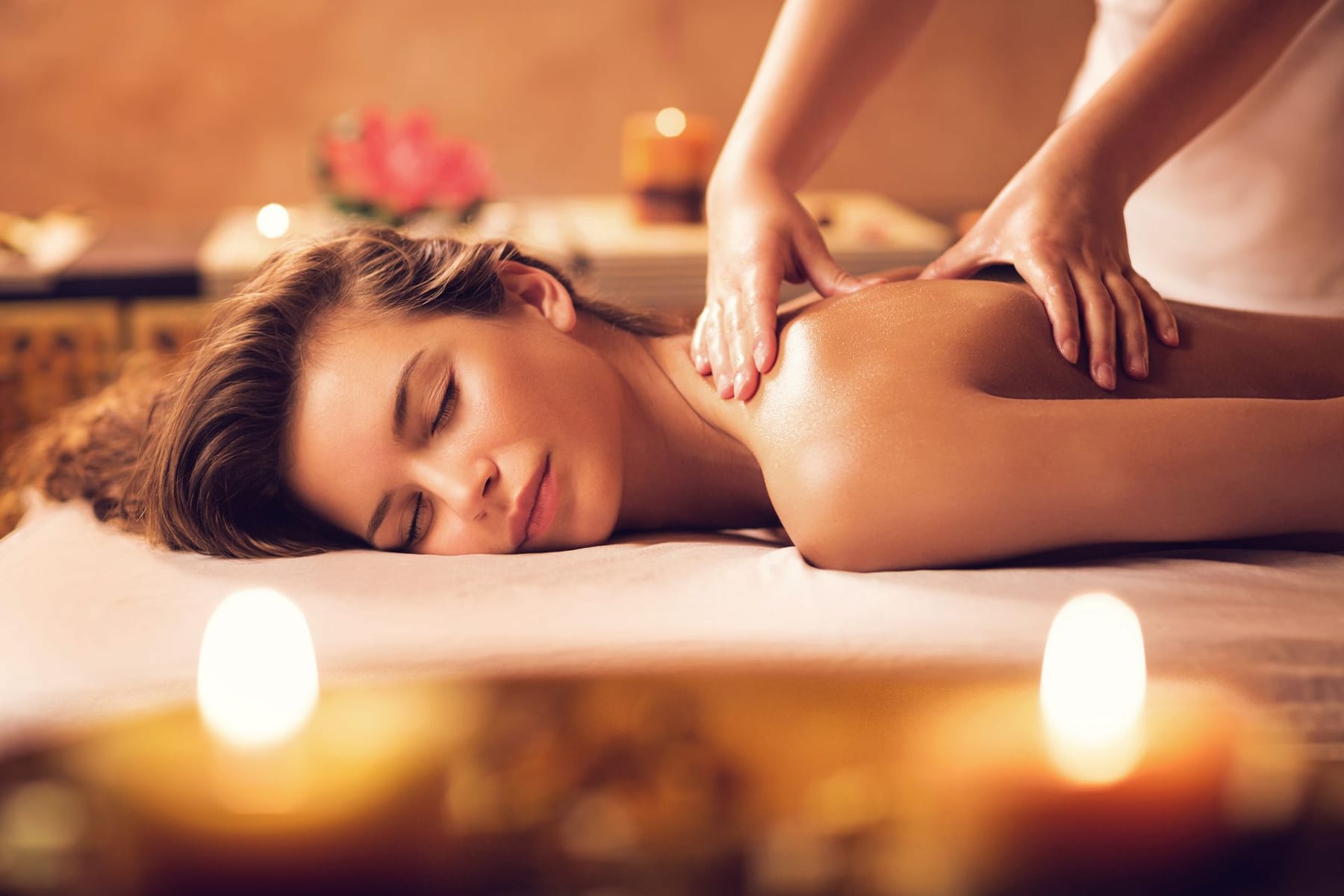 Massage therapist applying focused pressure through cream linen over a client shoulder.