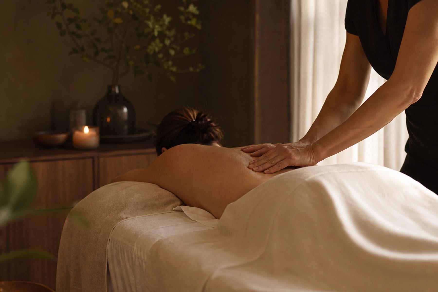 Massage therapist applying slow Swedish pressure over cream linen in a warm treatment room.